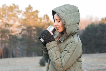 woman tourist in mountains at sunrise holding a thermos with tea or coffee and getting warm