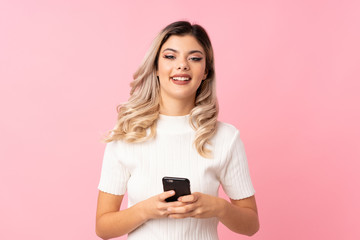 Teenager girl over isolated pink background sending a message or email with the mobile