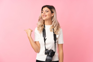 Teenager girl over isolated pink background with a professional camera and pointing to the side
