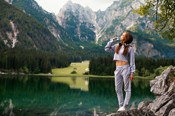 Naklejka premium Young sports woman drinks water on a mountain next to the lake