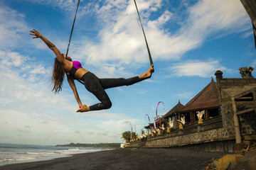 aero yoga beach workout - young attractive and athletic woman practicing aerial yoga exercise...