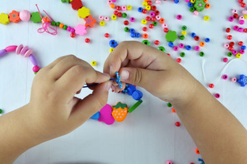 Little girl creates beads from colorful beads, last touches. Toy that develops the imagination of child. Process close-up