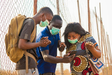 young black people wearing face masks having a conversation, checking something on a smartphone