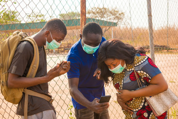 young black people wearing face masks having a conversation, checking something on a smartphone