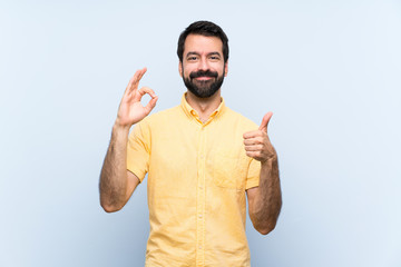 Young man with beard over isolated blue background showing ok sign and thumb up gesture