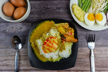 Thai rice noodles in grab curry sauce with vegetable and boiled eggs on wood table. Thai food style made with round flour, like noodles, eaten with chili paste.