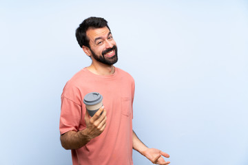 Fototapeta premium Young man with beard holding a take away coffee over isolated blue background smiling