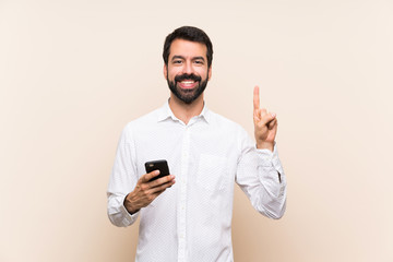 Young man with beard holding a mobile showing and lifting a finger in sign of the best