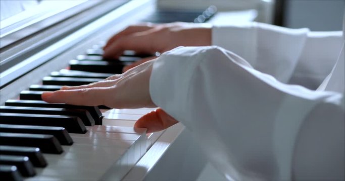 Woman or Girl Student or Professional Pianist Plays Classical Music on a Beautiful White Piano a Christmas Holiday Against Background of a Christmas tree and Blinking New Year Lights. Pianist's hands.