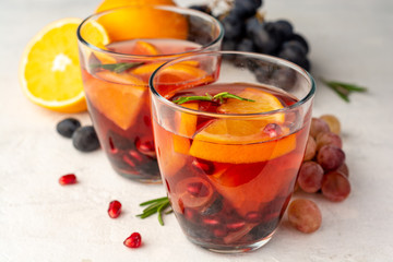 Homemade sangria with orange, grapes and pomegranate seeds in glasses on concrete background. Selective focus.