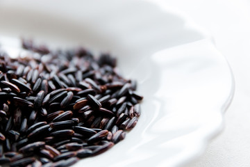 Black wild rice in a white plate close-up on a white background, selective focus