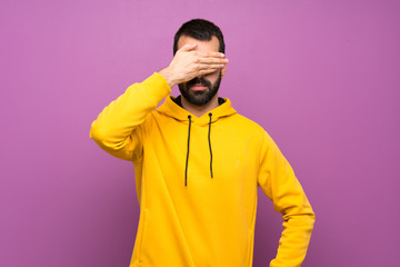 Handsome man with yellow sweatshirt covering eyes by hands. Do not want to see something