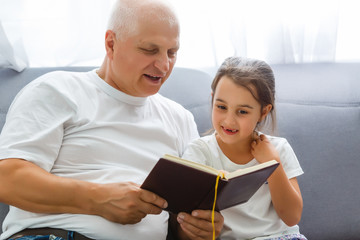 Happy little girl with grandfather reading story book at home