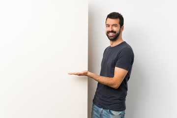 Young handsome man with beard holding a big empty placard presenting an idea while looking smiling towards