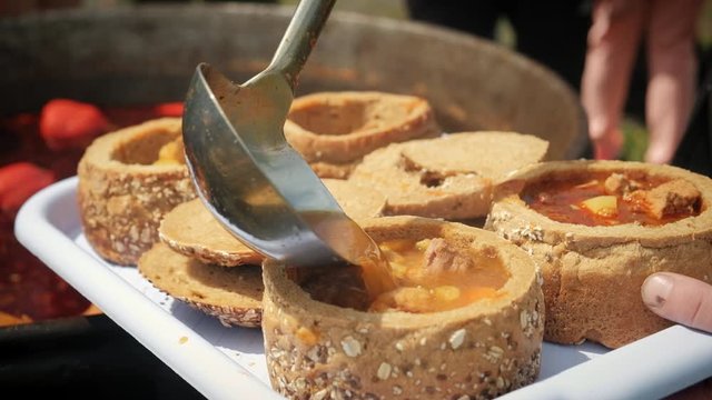 Gathering Bograch in bread. Bograch. Soup with paprika, meat, bean, vegetable, dumpling. Traditional Hungarian Goulash in cauldron. Meal cooked outdoors on an open fire. HD