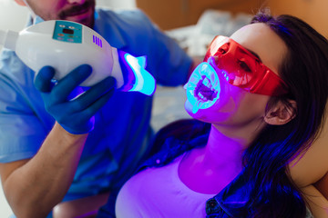 Photo of a young female patient at dentist in the clinic. Teeth whitening procedure with ultraviolet light UV lamp.