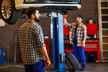 Fototapeta na wymiar two mechanics working together on the lifted car in workshop