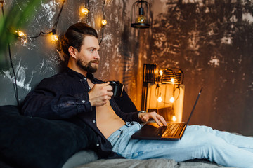 Handsome man in morning time, lying on bed with tablet and cup of coffee.