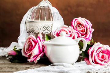 White cage and a tea pot with roses and decoration on a wooden table
