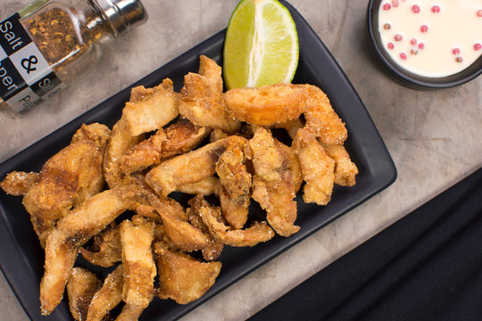 Fried Tilapia strips in a black platter with rose pepper sauce in background seen from above