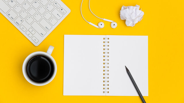 Blank spiral notepad with keyboard, supplies and pencil on bright yellow background. Top view office desk with notepad. Creative flat lay photo