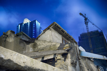 Old ruined house in front of modern buildings in construction.