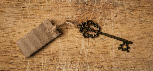 Old key with cardboard tag on wood background