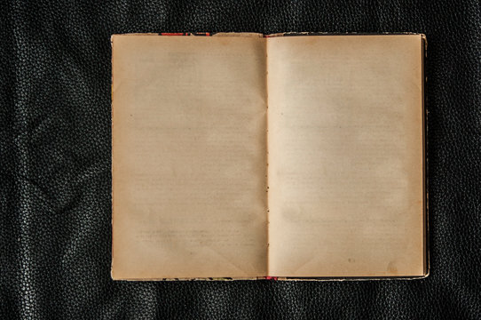 Open blank old book on black leather background, top view