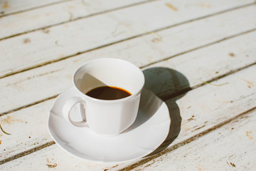 Cup of coffee on white wooden background with warm sunlight in the morning.