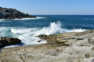 Seascape with waves breaking against the rocks and blue sky. Galicia, Spain.