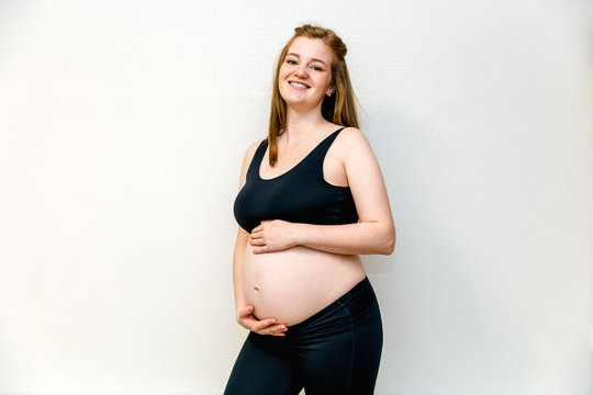 Image of pregnant woman in the black sport leggins and bra at thirty week (seven monthes) in the top and leggings, arms hugging her stomach. Pleasant expectation baby
