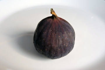 A close-up of a round purple fig, white background