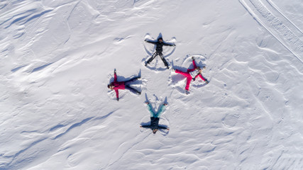 a group of young people in bright ski suits depict snow angels lying on the fresh snow in the form of a cross. four winter angels happy and energetic. Winter fun at the ski resort