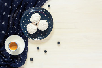 A pleasant morning with a Cup of coffee, marshmallows and blueberries on a white wooden table with a copy space decorated with blue textiles with stars evoking an American image and holiday