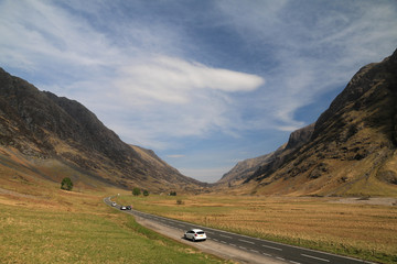 malownicza droga i jadące samochody pośród wysokich wzgórz w regionie highlands w szkocji - obrazy, fototapety, plakaty