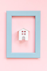 Simply design with miniature white toy house in blue frame isolated on pink pastel colorful trendy background. Mortgage property insurance dream home concept. Flat lay top view copy space