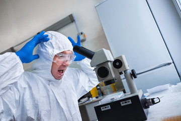 A biologist in a White protective suit and glasses works with a microscope in the laboratory. The...