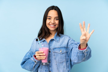 Obraz premium Young woman with strawberry milkshake over isolated blue background happy and counting four with fingers