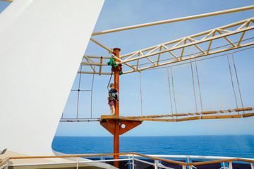 Happy little kid boy climbing on high rope course trail. Active child making adventure and action on family vacations. Challenge for brave kids.