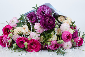 on a light background a bouquet of ranunculus and roses and transparent beads