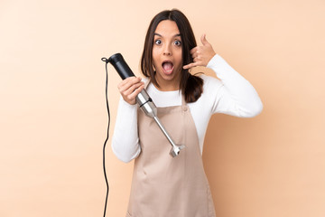 Young brunette girl using hand blender over isolated background making phone gesture. Call me back sign