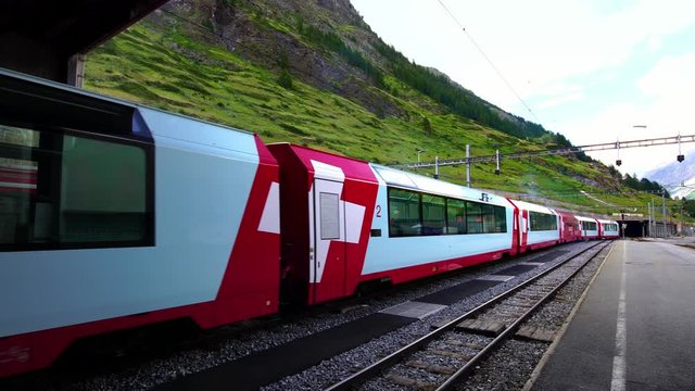 Swiss red Glacier Express train departing Zermatt, luxury alpine resort town by Matterhorn. Scenic railway across Swiss Alps to St. Moritz. Switzerland in summer, 4k.