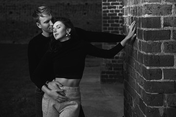 Romantic couple young beautiful sensual redhead woman and tall handsome blonde man posing in sunset sunlight on brick wall background in black and white