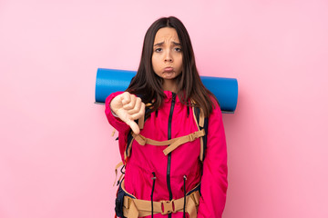 Young mountaineer girl with a big backpack over isolated pink background showing thumb down with negative expression
