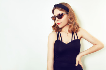 Hipster girl whole in a black dress, on a white background. Girl in unusual sunglasses and earrings. Fashion girl with a short haircut. Place for text