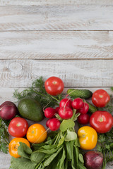 On a wooden table, onion, parsley, dill, tomatoes, radishes, avocados, cucumbers and free space for text