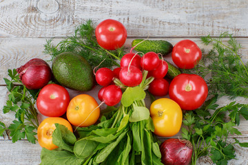 on the wooden table, onion, parsley, dill, tomatoes, radishes, avocados, cucumbers close up 