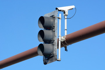 Black traffic light signal and traffic camera on overhead metal pole against blue sky