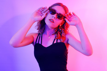 Beautiful girl in neon. Fashion photo of a short-haired girl, dancing, sun glasses. Girl in red and blue light posing.