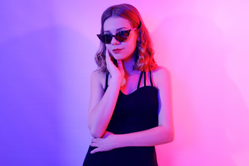 Beautiful girl in neon. Fashion photo of a short-haired girl, dancing, sun glasses. Girl in red and blue light posing.